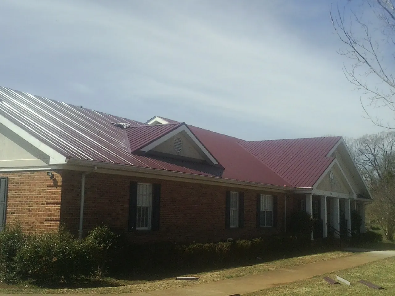 Red metal roof with gabled entries on a long brick building, from a Hail Damage Roof Repair job in Seward