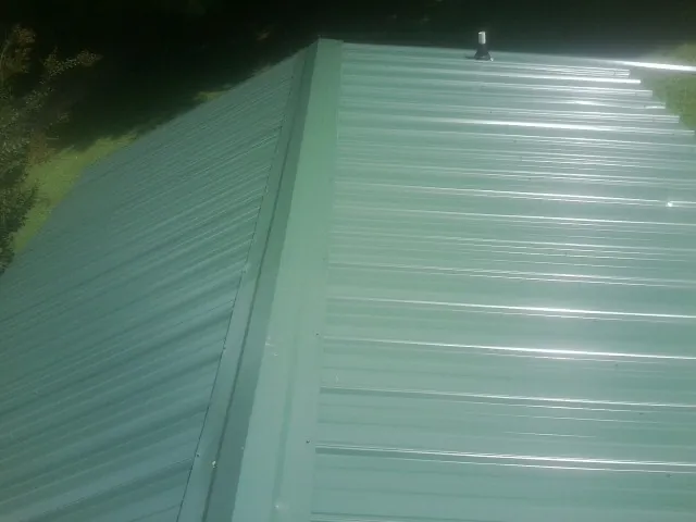 New green metal panels meeting at the ridge of a roof — Flat Roof Repair work by our crew in Seward