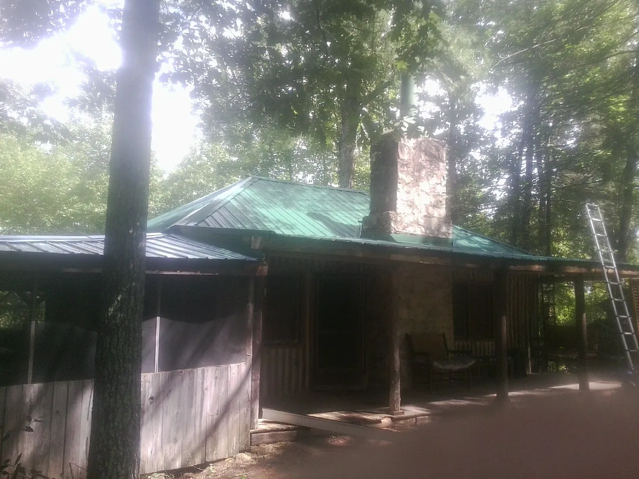 Green metal roof and stone chimney above a log cabin porch in Seward